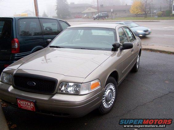 Tan 2001 Ford Crown Victoria parked next to a dark minivan. License plate frame says Cheyka Motors