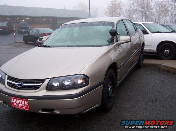Tan Chevrolet Impala with a police spotlight on the driver's side, parked next to a white car