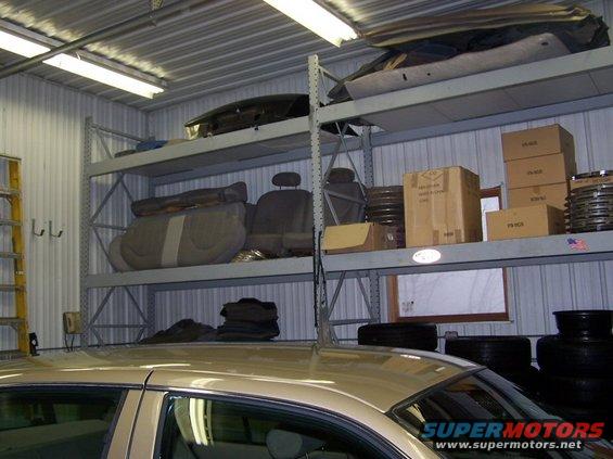 Car roof and interior visible, with shelves holding car seats, boxes, and tires in a garage