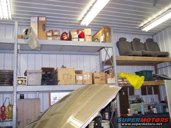 Tan car hood open in garage with shelves of parts and car seats above