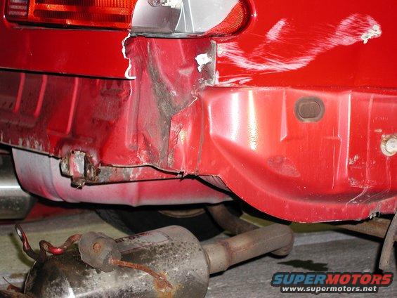 Damaged red car rear bumper with visible rust and a detached exhaust pipe below