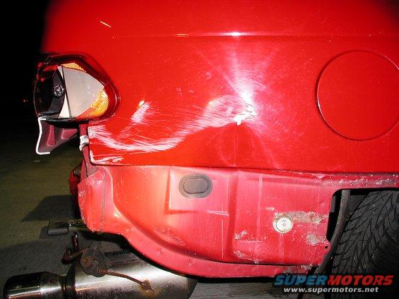 Red 1992 Ford Taurus rear bumper with significant damage, scratches, and rust. The taillight is broken. A spare tire is visible
