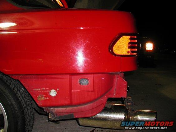 Close-up of a red car's rear corner, showing the taillight and bumper area. There's a Supermotors.net watermark at the bottom