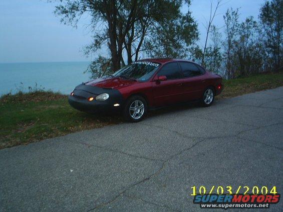 Red sedan with car bra parked by a lake, timestamp 10/03/2004
