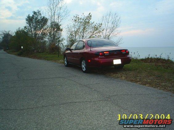 Red sedan parked on the side of a road next to a body of water