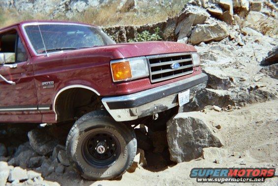 Maroon Ford Bronco navigating rocky terrain. It has a 'Bronco' badge on the fender