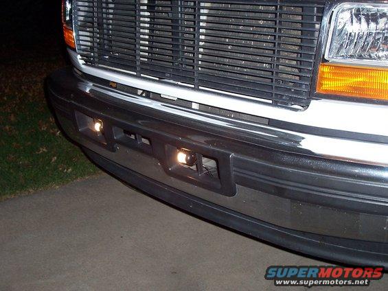 Front bumper with fog lights and chrome trim, grille and headlight visible