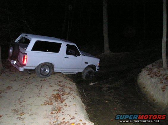 White Ford Bronco on a dirt trail at night, with a spare tire mounted on the rear