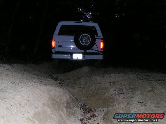 White 1996 Ford Bronco rear view on dirt trail at night