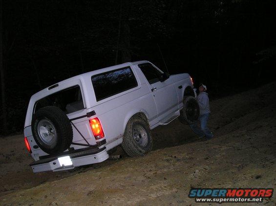 White 1996 Ford Bronco on a dirt hill at night, with a person near the front wheel