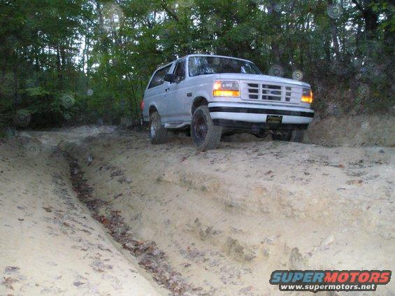 White SUV with a grille from the early to mid-1990s on a sandy, rutted trail