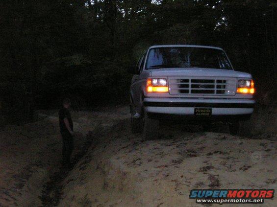 White Ford Bronco with headlights on, front view. License plate reads 'PURDUE ALUMNI'