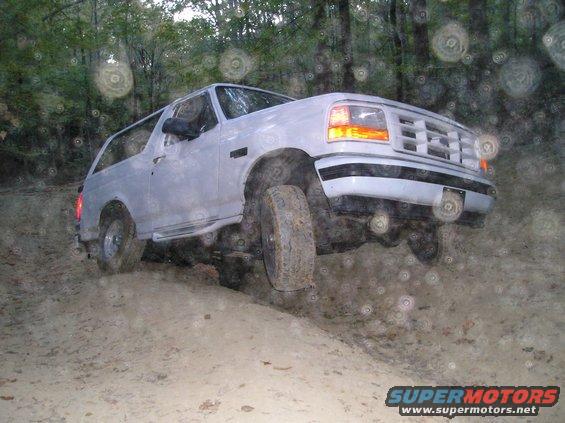 1996 Ford Bronco driving on a dirt trail with trees in the background