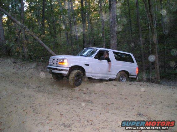 White Ford Bronco driving on a dirt trail in a forest