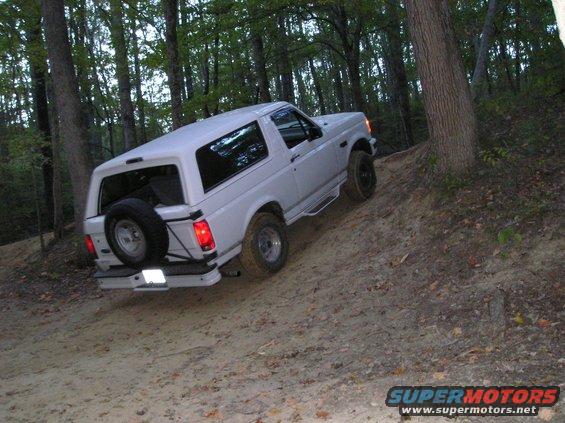 White 1996 Ford Bronco driving up a dirt hill in a forest