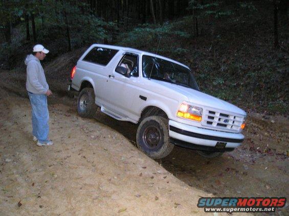 White 1996 Ford Bronco driving on a dirt trail in the woods