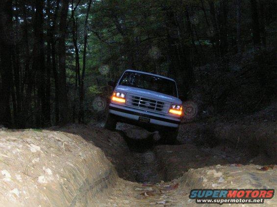 White 1992 Ford Bronco navigating a rutted dirt trail through woods