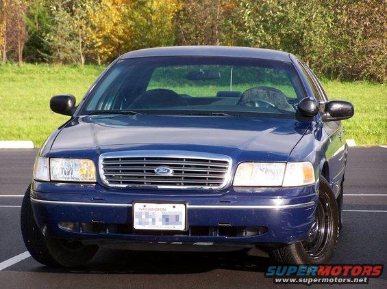 Front view of a blue Ford Crown Victoria parked outside with trees in the background