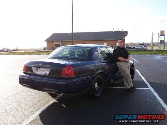 Dark blue 2001 Ford Crown Victoria, rear 3/4 view, with a man leaning on the driver's side