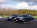 1998 Ford Crown Victoria - Two dark blue sedans, likely police cruisers, are parked side-by-side in an outdoor lot under a cloudy sky.