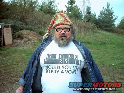 Man wearing a colorful hat, glasses, and a t-shirt that says 'G F CK Y RS LF WOULD YOU LIKE TO BUY A VOWEL?'