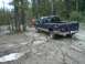 1999 Ford F-250 - Two pickup trucks navigate a challenging muddy trail surrounded by trees.