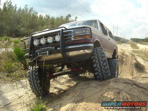 Modified Ford Bronco with large tires and brush guard driving on a dirt hill