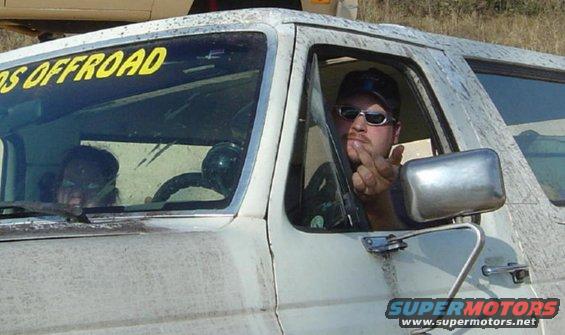 Dirty white SUV interior with driver giving the finger. Yellow 'OS OFFROAD' sticker on windshield