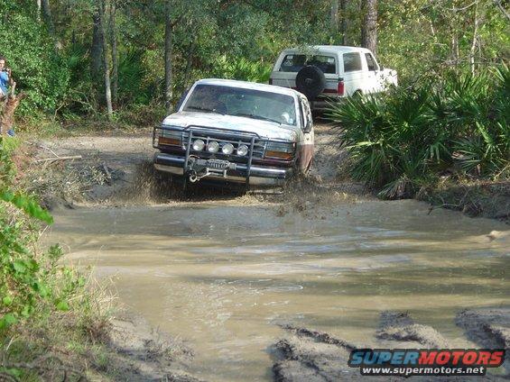 Two Ford Broncos navigating a muddy trail, one in the foreground splashing water