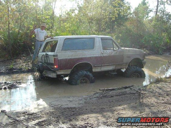 Two-tone red and white Ford Bronco stuck in mud, front 3/4 view