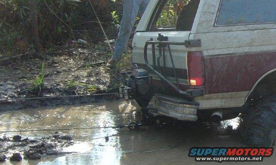 Rear view of a 1993 Ford Bronco stuck in mud, with a winch attached