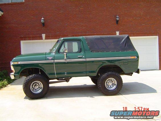 Green Ford Bronco with a black soft top parked in front of a brick house with garage doors