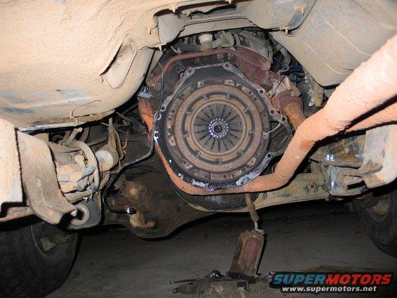 Underside view of a vehicle's clutch assembly and part of the transmission, with exhaust pipes visible