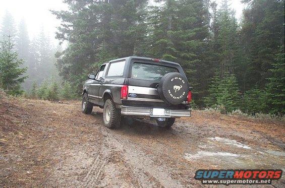 1995 Ford Bronco parked on a muddy, wooded trail. Spare tire on the back has 'Ford Bronco' text