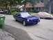 1965 Ford Mustang - A blue coupe is parked on a residential street next to a green trash can, with a covered vehicle behind it.