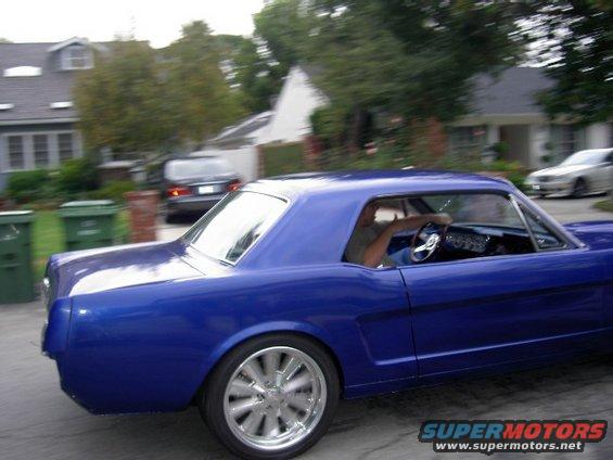 Blue 1965 Ford Mustang coupe driving past houses, side view