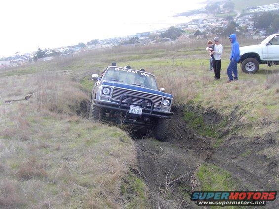 Blue pickup truck with "DREAM ON" on windshield driving through mud, license plate SF51450