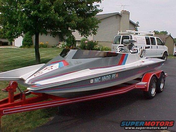 Gray and white speed boat on a red trailer, with a white van in the background