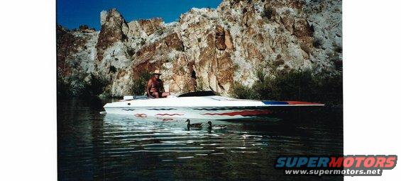 Person sitting on a white and red speed boat with ducks in the water, rocky cliffs in background