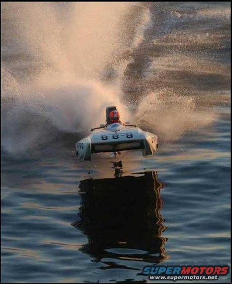 White powerboat with red-helmeted driver speeds through water, creating a large spray