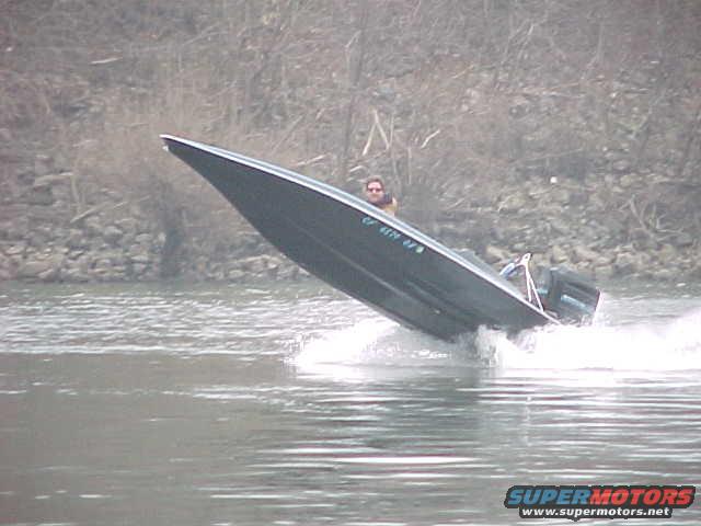 Dark boat with a person at the helm speeds through water, kicking up spray
