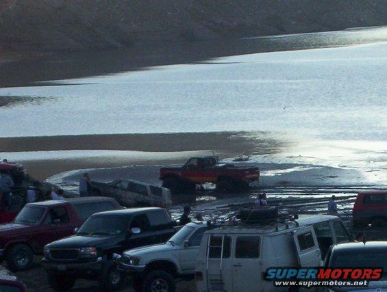 Several trucks and vans parked on muddy ground near a body of water