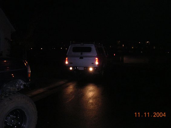 White pickup truck with a camper shell, rear view at night. Two round reverse lights are illuminated