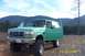 1996 Ford Bronco - This lifted green Ford Bronco is parked outdoors with its doors open, set against a backdrop of forested hills.