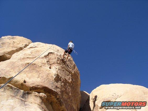 climber rappelling down a rock face with a rope against a blue sky