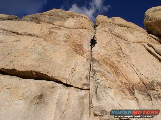 Rock climber ascending a narrow crack on a large rock face under a blue sky
