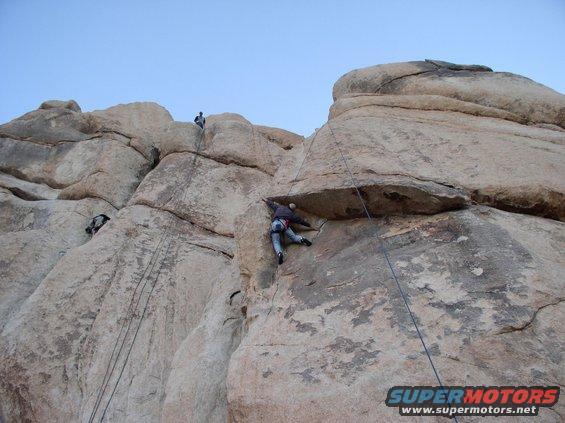 People climbing a large rock formation with ropes and harnesses