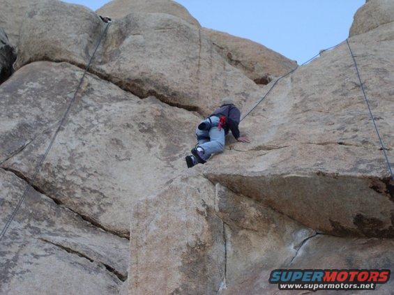 Rock climber ascending a large boulder with ropes