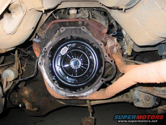 Underside view of a vehicle's transmission bell housing with a new clutch installed. A label on the clutch reads 'H29S'