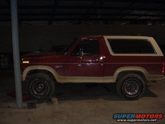 Side view of a red and white 1986 Ford Bronco with off-road tires